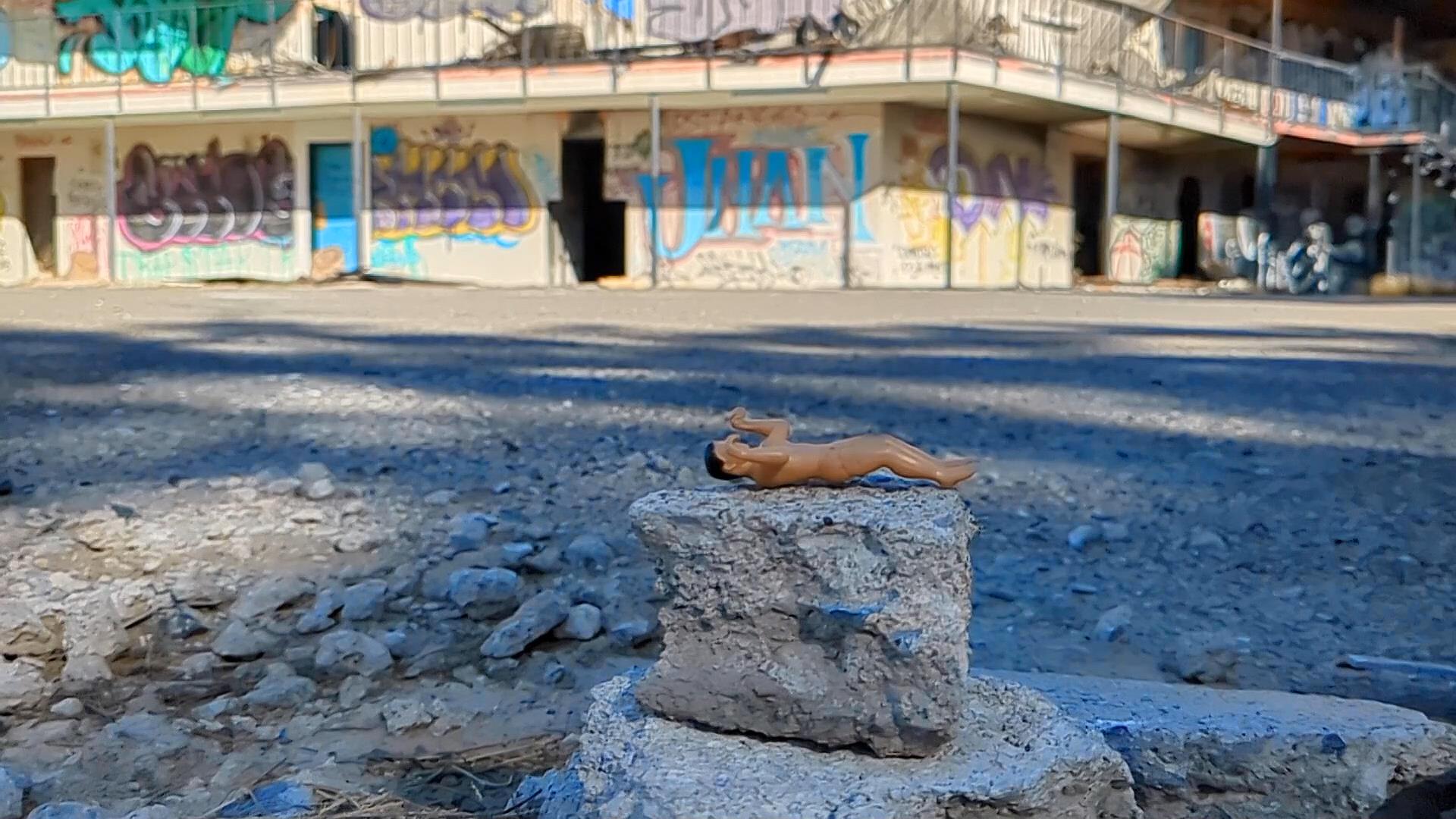 singular tiny man awaits his fate, lying on rocks in front of an abandoned hotel