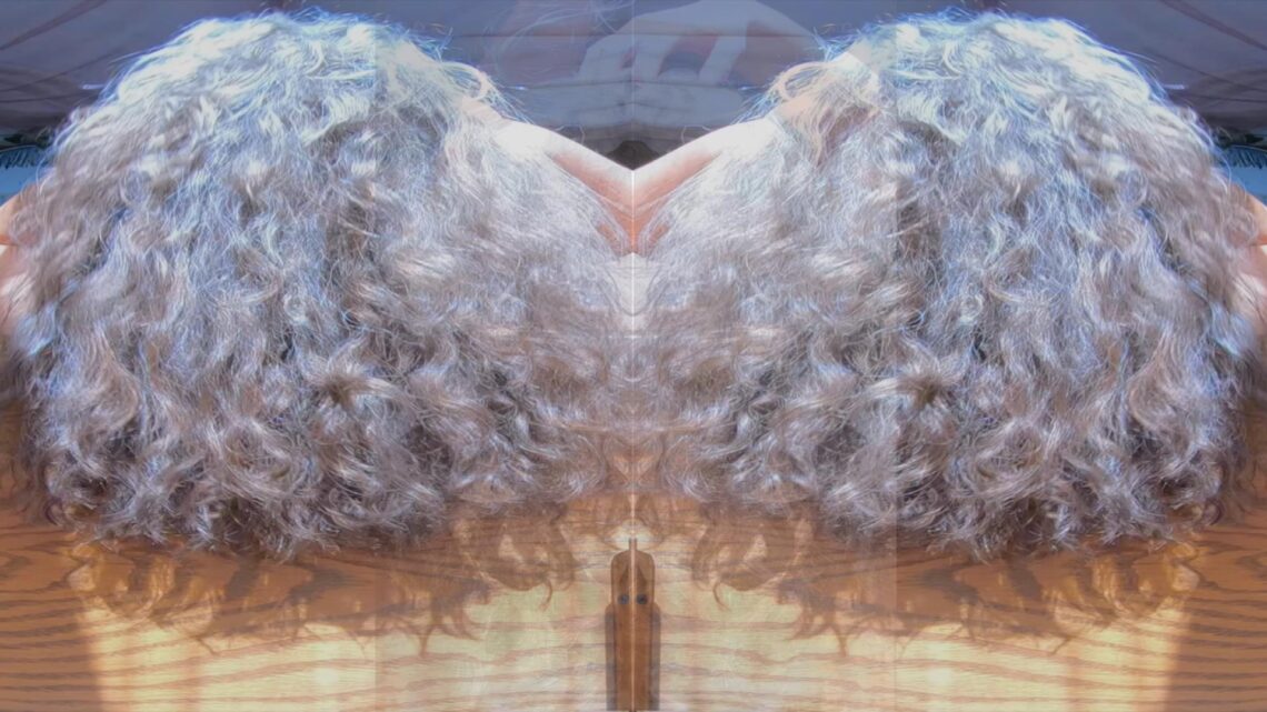 Mirrored image of thick, long, curly grey and silver hair, an asset of Miss Devora Moore OctoGoddess. Screenshot from Obsessed with My Hair.